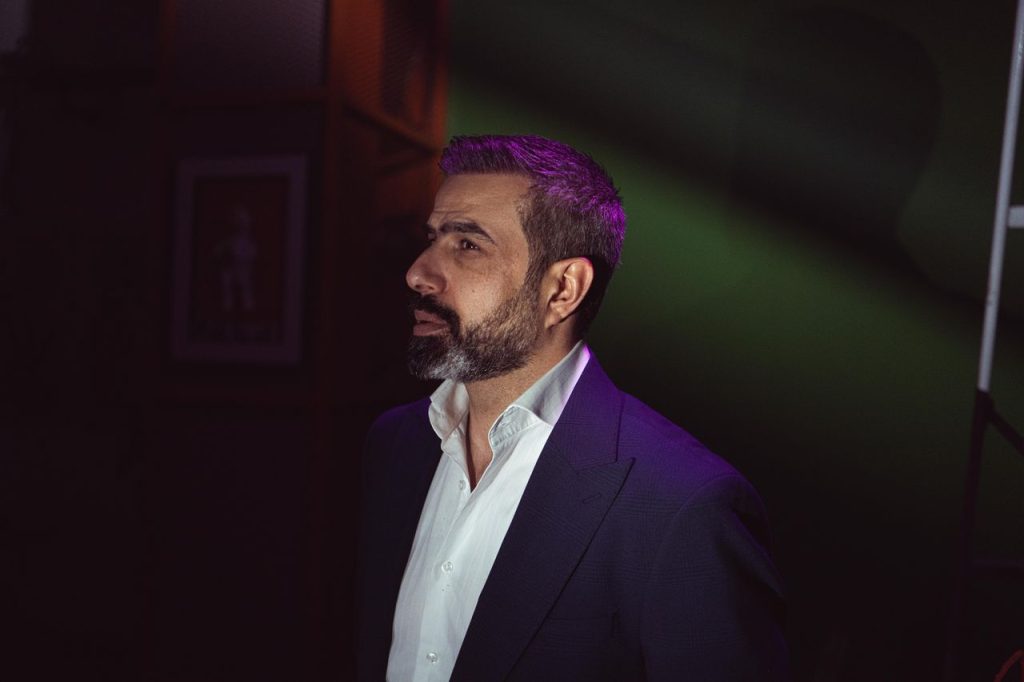 Profile of a bearded man in a suit captured in a moody, dramatic setting.